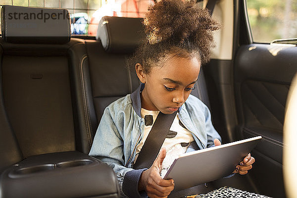 Mädchen benutzt digitales Tablet beim Sitzen im Elektroauto