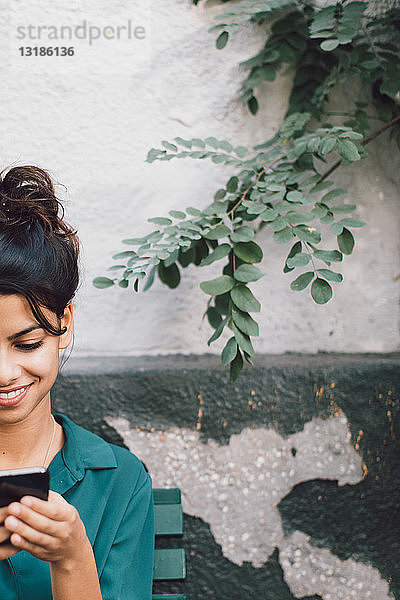 Ausgeschnittenes Bild einer jungen Frau  die ein Mobiltelefon an der Wand benutzt