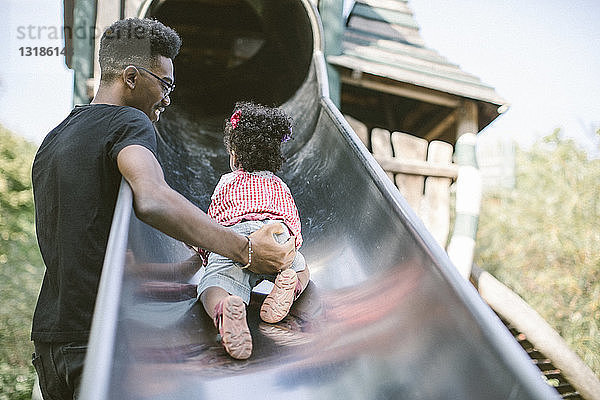 Vater unterstützt Tochter  die auf einer Rutsche auf dem Spielplatz hochkrabbelt