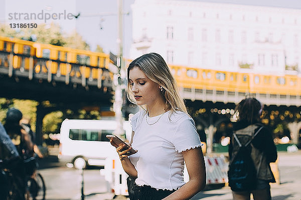 Junge Frau benutzt Mobiltelefon beim Gehen auf der Straße in der Stadt
