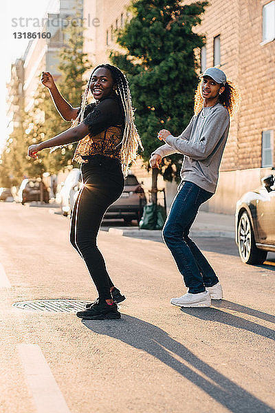 Lächelnde Freunde in voller Länge tanzen auf der Straße in der Stadt