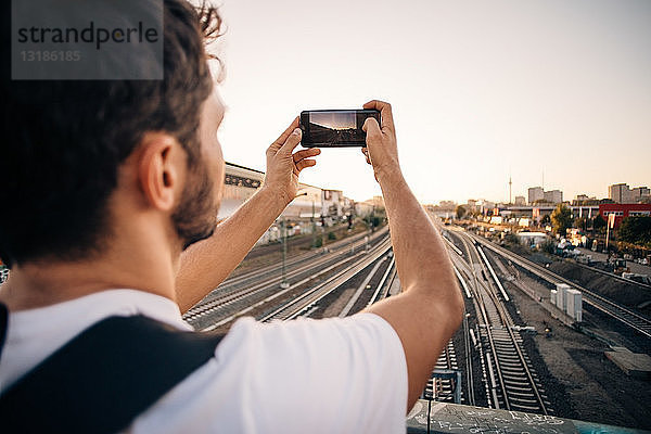 Junger Mann fotografiert per Handy über Eisenbahnschienen in der Stadt