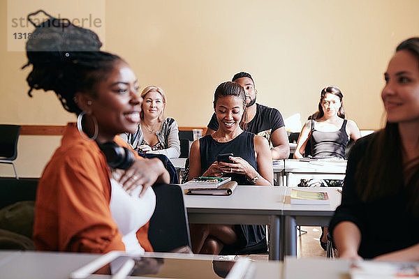 Reife Frau benutzt Smartphone  während sie mit Klassenkameraden im Sprachunterricht sitzt
