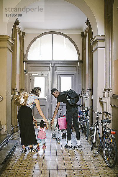 Mutter und Vater assistieren der Tochter in voller Länge beim Gehen im Korridor