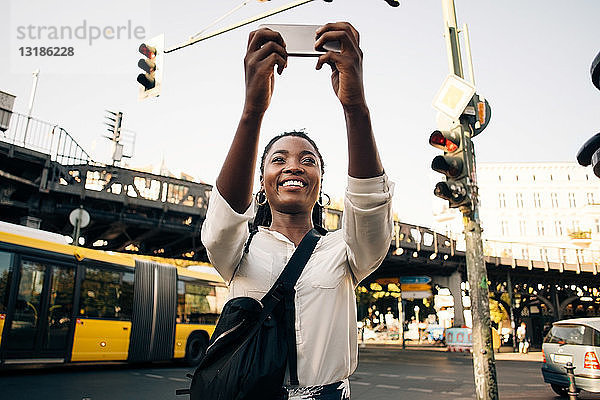 Lächelnde junge Frau fotografiert per Handy  während sie in der Stadt auf der Straße steht