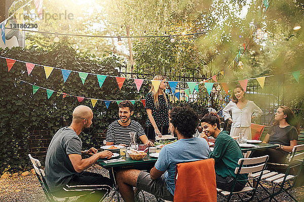 Glückliche multiethnische Freunde unterhalten sich beim Abendessen während einer Gartenparty