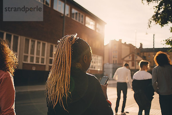 Rückansicht der Textnachrichten von Teenager-Mädchen auf einem Smartphone beim Spaziergang mit Freunden in der Stadt