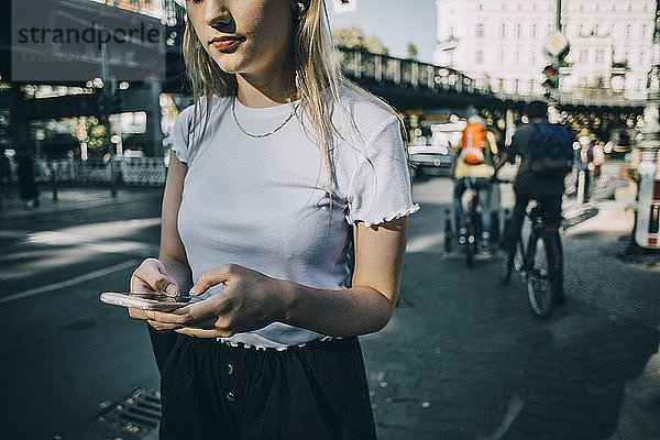 Mitschnitt einer jungen Frau  die ein Smartphone benutzt  während sie in der Stadt auf dem Bürgersteig steht