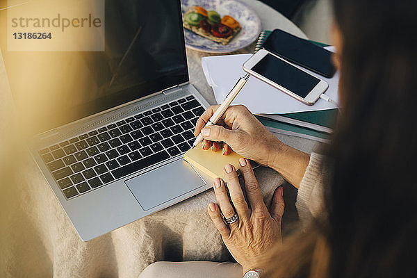 Ausgeschnittene Frau schreibt auf Klebezettel über Laptop am Tisch