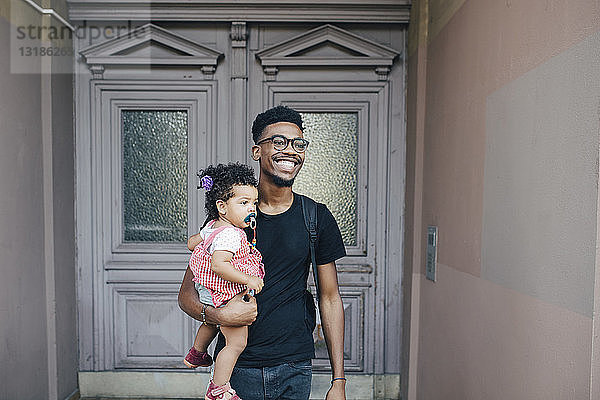 Lächelnder Vater schaut weg  während er seine Tochter gegen eine geschlossene Tür trägt