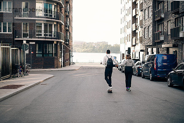 Freunde in voller Länge skateboarden gemeinsam auf der Straße in der Stadt