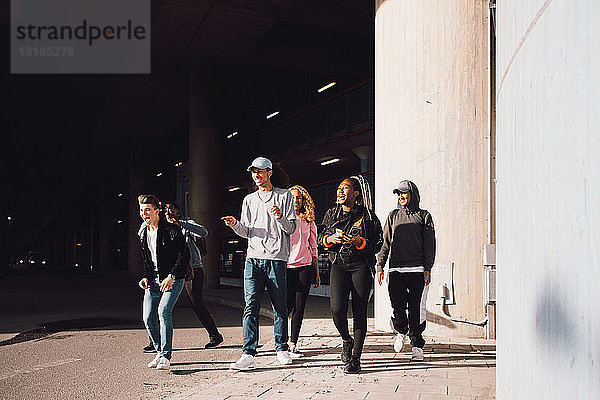 Glückliche Freunde schauen weg  wenn sie an einem sonnigen Tag auf der Straße unter der Unterführung in der Stadt spazieren gehen