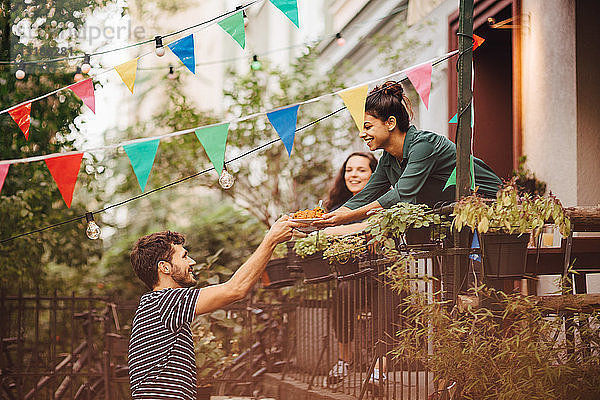 Lächelnde junge Frau gibt einem Freund während einer Gartenparty vom Balkon aus Essen