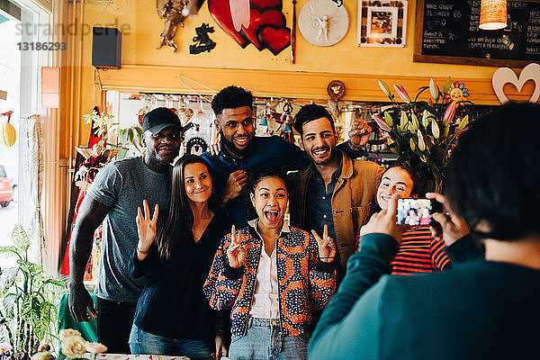 Junger Mann fotografiert fröhliche multi-ethnische Freunde  die während des Brunch im Restaurant stehen