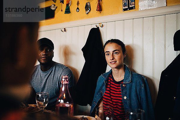 Junge Frau sitzt neben einem Mann  während sie während einer Dinnerparty eine Freundin im Restaurant anschaut