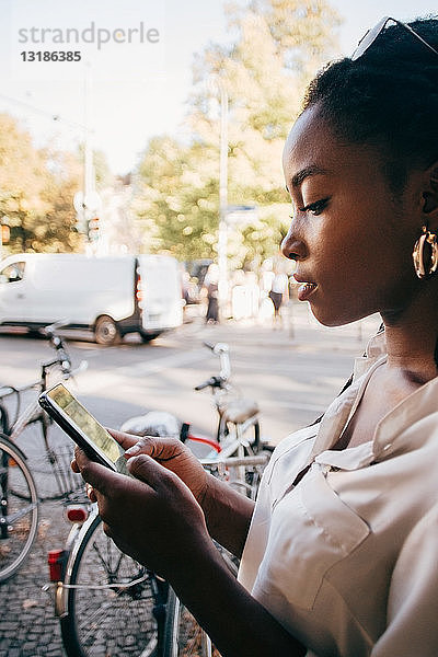 Junge Frau benutzt Smartphone  während sie in der Stadt auf dem Bürgersteig steht