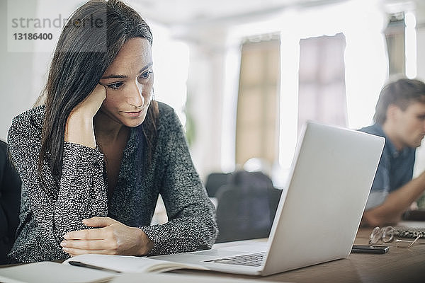 Müde Geschäftsleute schauen auf den Laptop  während sie im Kreativbüro am Schreibtisch sitzen