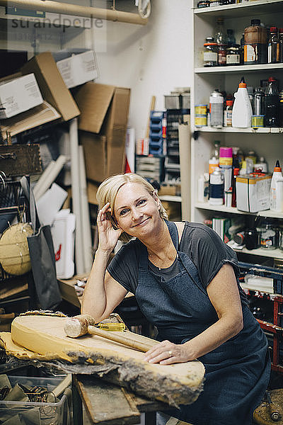 Porträt einer selbstbewussten Polsterin  die an der Werkbank in einer Werkstatt sitzt