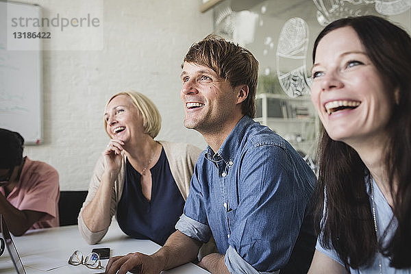 Lächelnde kreative Geschäftsleute  die während einer Besprechung im Konferenzraum sitzen und zuhören