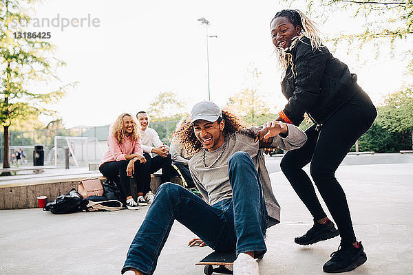 Teenager drängt glücklichen Mann auf Skateboard beim Spielen im Park