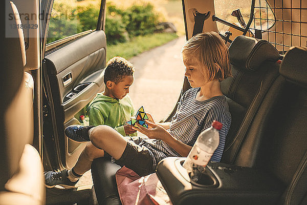 Mädchen spielt Puzzle-Würfel  während sie im Auto sitzt  neben ihrem Bruder im Park