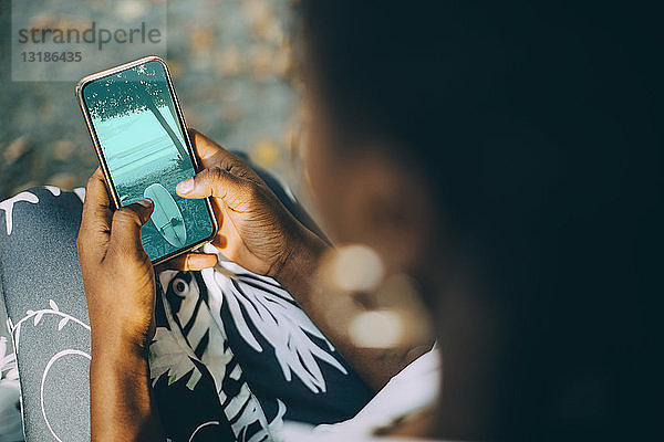 Hochwinkelaufnahme einer jungen Frau  die ein Strandfoto auf einem Smartphone betrachtet