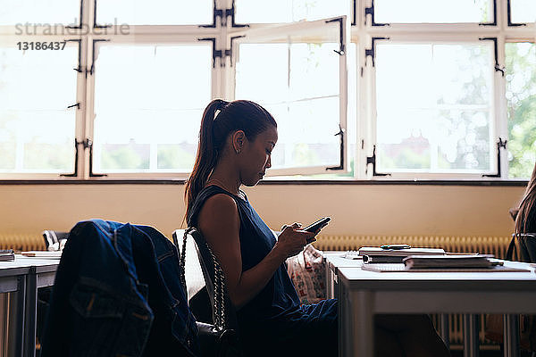 Seitenansicht einer Frau  die ein Mobiltelefon benutzt  während sie in einer Sprachschule sitzt