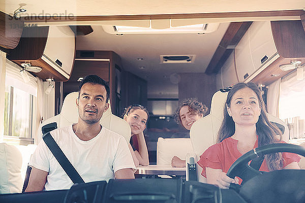 Glückliche Familie schaut weg  während sie im Wohnwagen sitzt  von der Windschutzscheibe aus gesehen