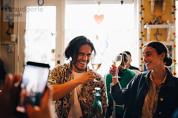 Mann fotografiert fröhliche junge Freunde  die während des Brunch im Restaurant einen feierlichen Toast ausbringen