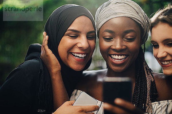 Lächelnde multiethnische Freunde  die im Hinterhof stehen und auf ihr Handy schauen