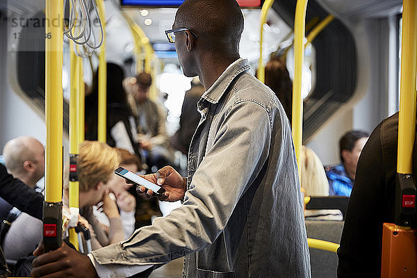 Seitenansicht eines männlichen Pendlers mit Mobiltelefon im Bus stehend