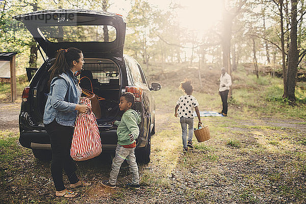 Familie entlädt Gepäck aus dem Kofferraum eines Elektroautos am Parkplatz