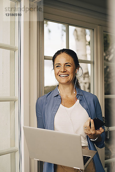 Porträt einer lächelnden Frau  die in der Ferienvilla mit dem Laptop über Kopfhörer spricht
