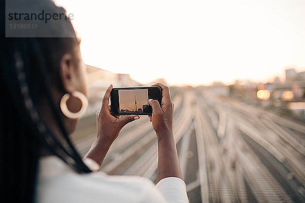 Junge Frau fotografiert Fernsehturm bei Sonnenuntergang per Handy