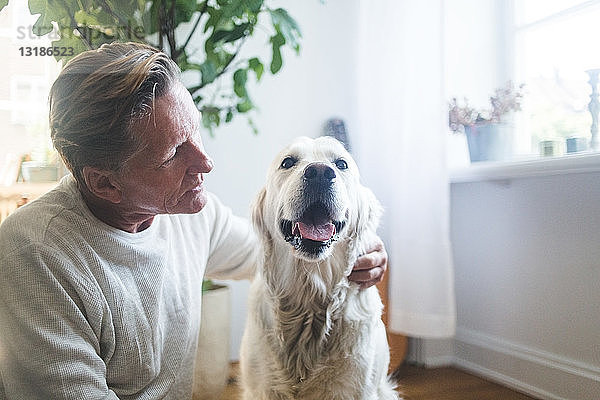 Rentner umarmt sich  während er den Hund im Wohnzimmer anschaut