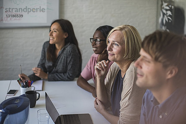 Lächelnde kreative Geschäftsleute hören zu  während sie im Konferenzraum sitzen