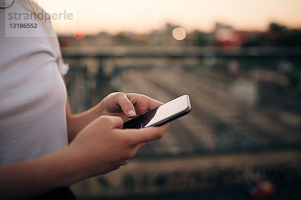 Ein Teil einer jungen Frau  die ein Smartphone benutzt  während sie auf einer Brücke in der Stadt steht