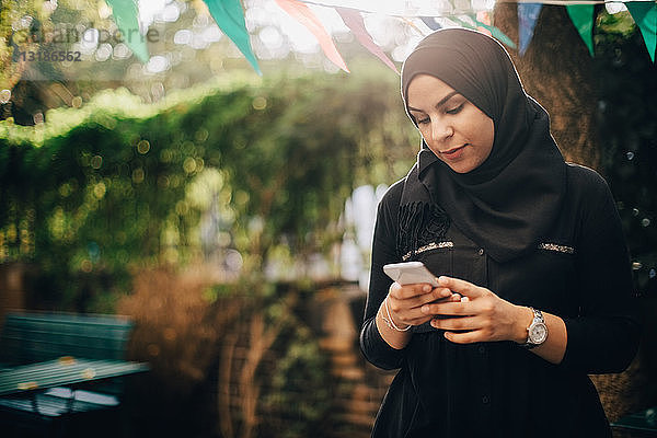 Junge Frau im Hidschab benutzt Smartphone während Gartenparty