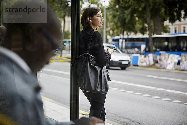 Geschäftsfrau schaut weg  während sie mit einem Pendler in der Stadt an einer Bushaltestelle steht