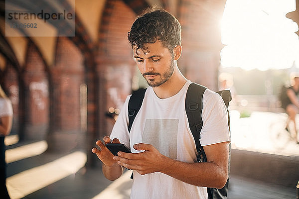 Junger Mann benutzt Mobiltelefon  während er auf einem Fußweg in der Stadt steht