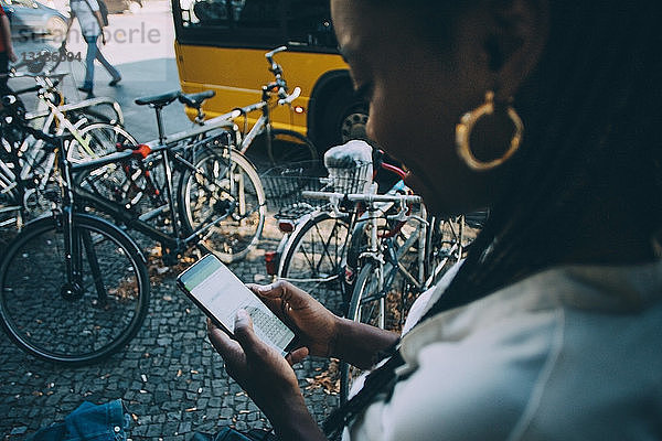 Junge Frau  die in der Stadt auf dem Bürgersteig stehend Textnachrichten über ein Smartphone verschickt