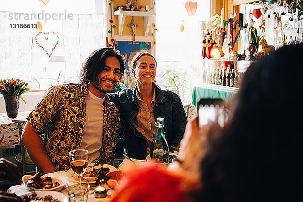 Junge Frau fotografiert lächelnde Freunde  die während des Brunch am Tisch im Restaurant sitzen