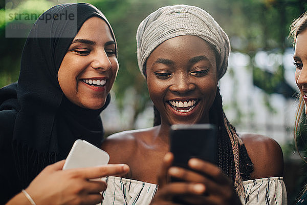 Glückliche multiethnische Freundinnen  die im Hinterhof stehen und auf ihr Handy schauen