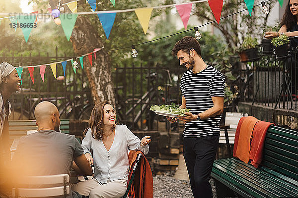 Lächelnde junge Frau im Gespräch mit einem Freund  der während einer Gartenparty Essen trägt