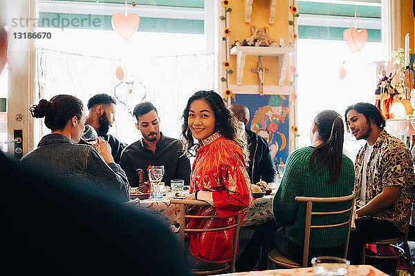 Porträt einer lächelnden jungen Frau  die während einer Brunch-Party im Restaurant inmitten multiethnischer Freunde sitzt