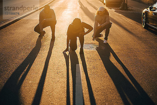 Freunde in voller Länge  die bei Sonnenuntergang im Sonnenlicht auf der Straße tanzen