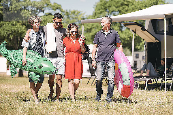 Glückliche Familie mit aufblasbaren Ringen  die in Wohnwagen auf Grasfeld spazieren gehen