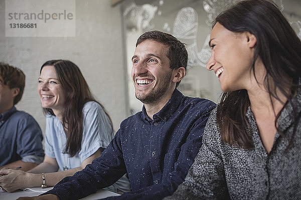 Lächelnde Geschäftsleute hören zu  während sie während der Sitzung im Sitzungssaal sitzen