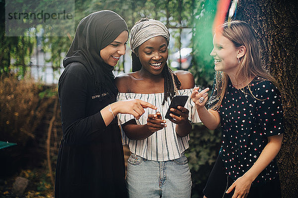 Lächelnde multiethnische Freundinnen  die im Hinterhof stehen und auf ihr Handy schauen