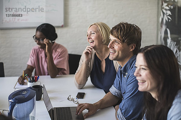 Kreative Geschäftsleute lächeln  während sie am Konferenztisch im Sitzungssaal sitzen